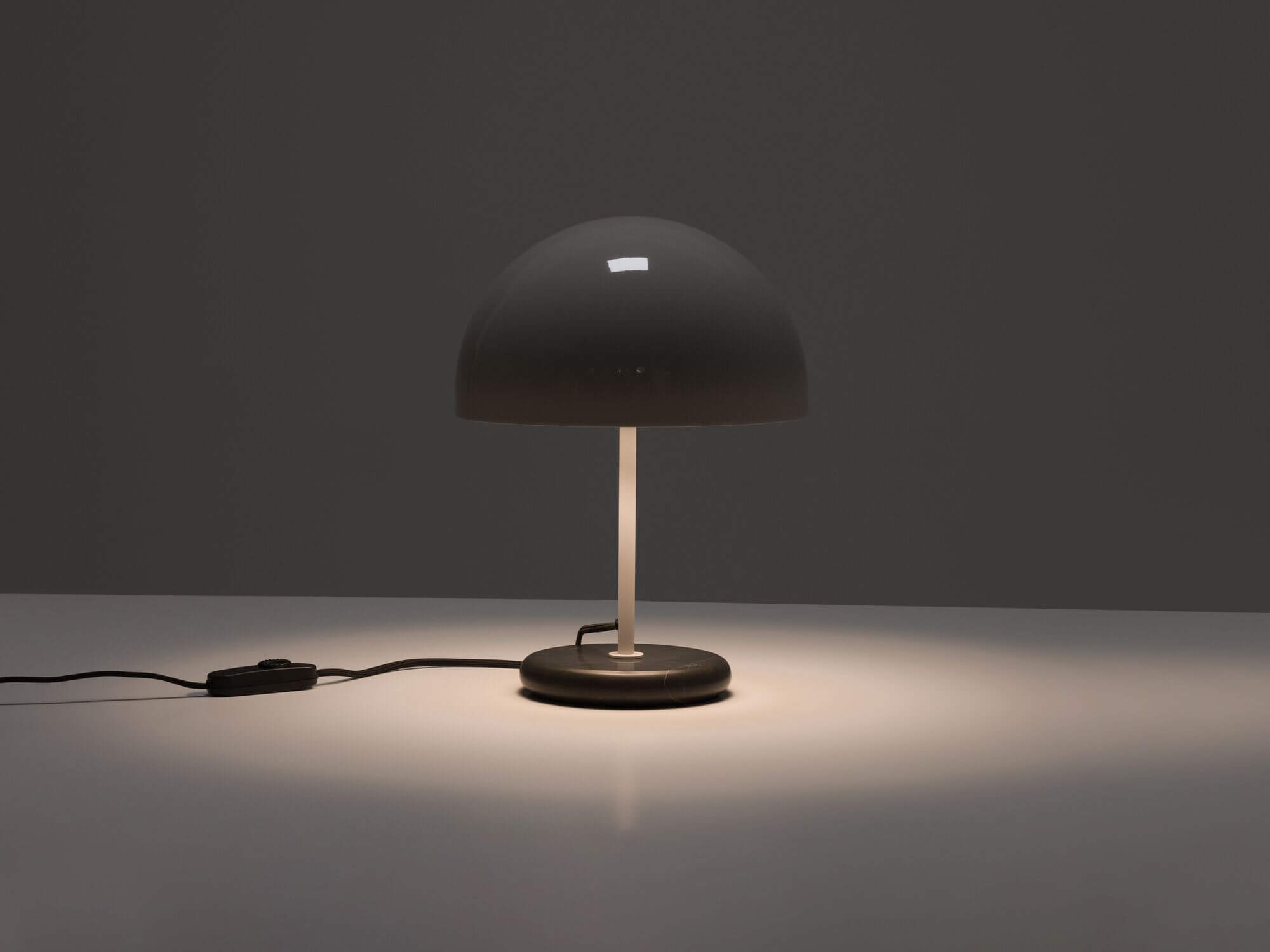 Round grey shade table lamp with light on in the dark front view